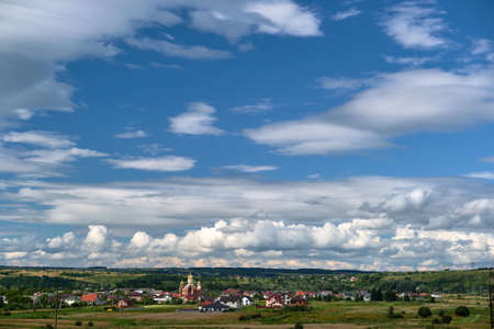 Bright landscape of white puffy cumulus clouds on blue clear sky over rural area.の写真素材