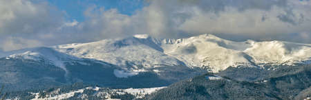 Winter landscape with high mountain hills covered with evergreen pine forest after heavy snowfall on...