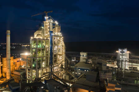 Aerial view of cement factory with high concrete plant structure and tower cranes at industrial production area at night. Manufacture and global industry concept.の写真素材