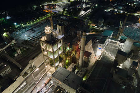 Aerial view of cement factory with high concrete plant structure and tower cranes at industrial production area at night. Manufacture and global industry concept.の写真素材