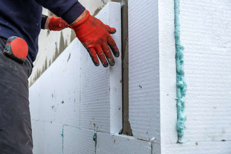Construction worker installing styrofoam insulation sheets on house facade wall for thermal protection.の写真素材