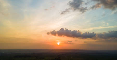 Bright colorful sunset sky with setting sun and vibrant clouds over dark landscape.の写真素材