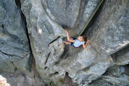 Determined boy climber clambering up steep wall of rocky mountain. Child overcoming difficult route....