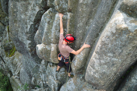 Determined climber clambering up steep wall of rocky mountain. Sportsman overcoming difficult route....