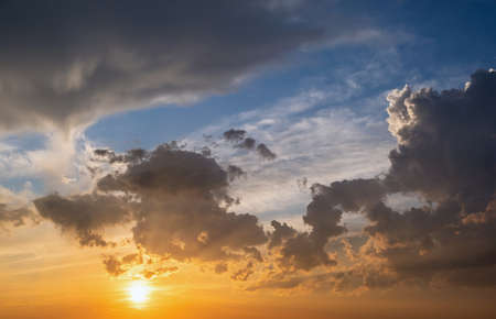 Dramatic sunset landscape with puffy clouds lit by orange setting sun and blue sky.の写真素材