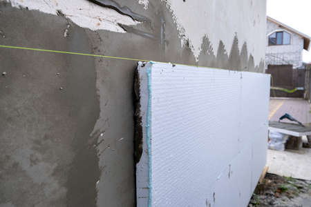 Installation of styrofoam insulation sheets on house facade wall for thermal protection.