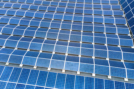 Aerial view of solar power plant with blue photovoltaic panels mounted on industrial building roof for producing green ecological electricity. Production of sustainable energy concept.の写真素材