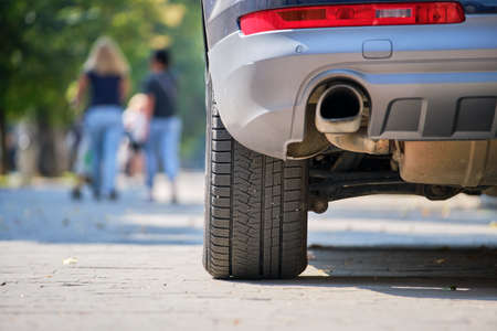 Close up of car rear wheel and exhaust pipe parked on city street side.の写真素材