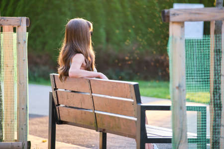 Lonely young woman sitting alone on lake shore bench enjoying warm summer evening. Wellbeing and relaxing in nature concept.の写真素材