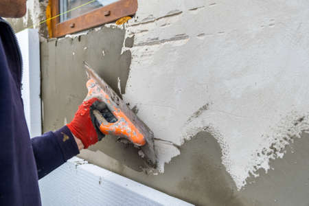 Construction worker covering house wall with adhesive cement glue berore installing styrofoam insulation sheets for thermal protection.の写真素材