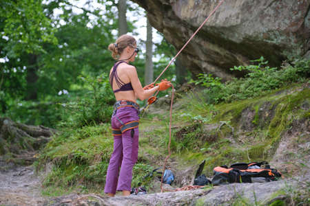 Woman belays her partner climber with belaying device and rope. Climber's helper holding equipment...
