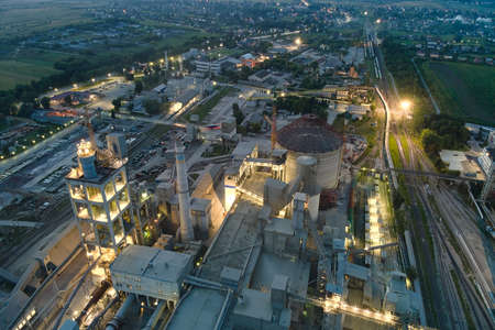 Aerial view of cement factory with high concrete plant structure and tower cranes at industrial production area at night. Manufacture and global industry concept.のeditorial素材