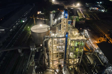 Aerial view of cement factory with high concrete plant structure and tower cranes at industrial production area at night. Manufacture and global industry concept.のeditorial素材