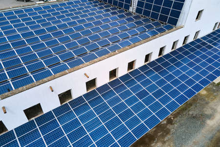 Aerial view of blue photovoltaic solar panels mounted on industrial building roof for producing...