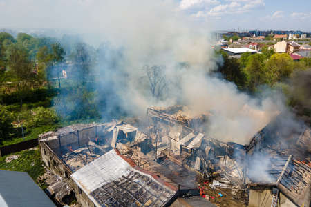 Aerial view of ruined building on fire with collapsed roof and rising dark smoke.
