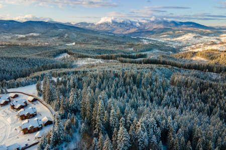 Aerial winter landscape with small village houses between snow covered forest in cold mountains in the evening.の写真素材
