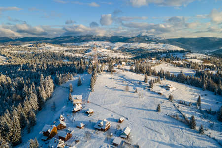 Aerial winter landscape with small village houses between snow covered forest in cold mountains in the evening.の写真素材