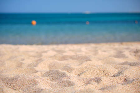 Close up of clean yellow sand surface covering seaside beach with blue sea water on background. Travel and vacations conceptの写真素材