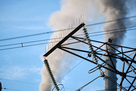 High voltage electric pylons against coal power plant high pipes with black smoke moving upwards polluting atmosphere. Production of electrical energy with fossil fuel conceptの写真素材
