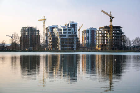 Tower cranes and high residential apartment buildings under construction on lake shore. Real estate developmentの写真素材