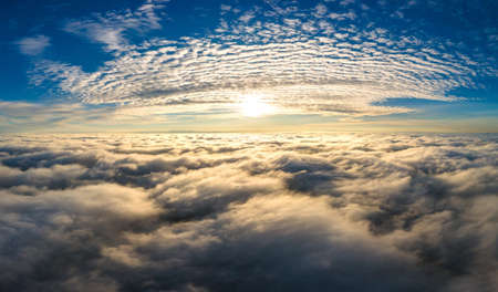 Aerial view of bright yellow sunset over white dense clouds with blue sky overheadの写真素材