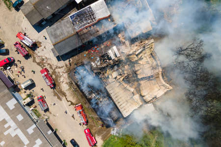 Aerial view of firefighters extinguishing ruined building on fire with collapsed roof and rising dark smokeの写真素材