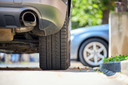 Close up of car rear wheel and exhaust pipe parked on city street side