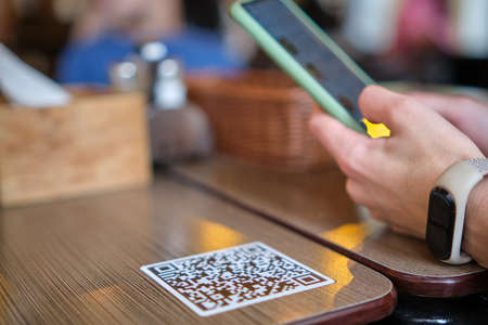 Closeup of guest hand ordering meal in restaurant while scanning qr code with mobile phone for online menuの素材 [FY310177978941]