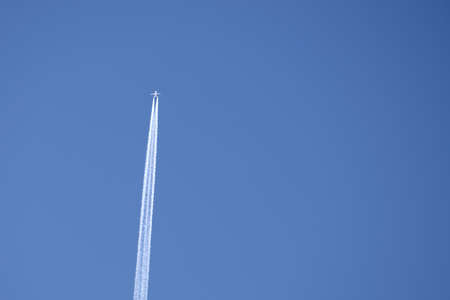 Distant passenger jet plane flying on high altitude on clear blue sky leaving white smoke trace of contrail behind. Air transportation conceptの写真素材