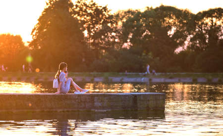 Young woman in casual outfit relaxing on lake side on warm evening. Summer vacations and travelling...