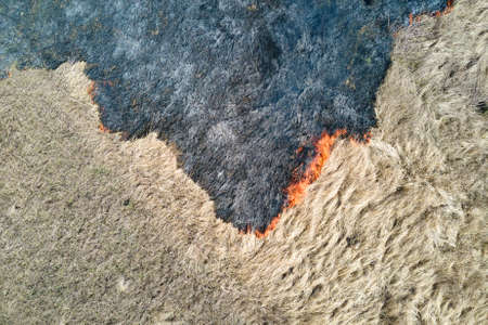 Aerial view of grassland field burning with red fire during dry season. Natural disaster and climate...