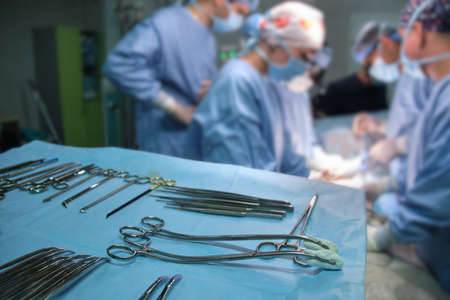 Closeup of surgical tools on table and team of surgery doctors operating a patient in hospital roomの写真素材