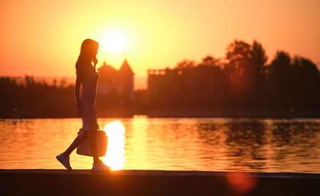 Lonely pedestrian woman walking alone on lake side on warm evening. Solitude and relaxation conceptの写真素材
