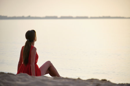 Lonely young woman sitting on ocean sandy beach by seaside enjoying warm tropical evening.の写真素材
