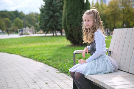 Portrait of pretty child girl sitting on park bench outdoors.の写真素材