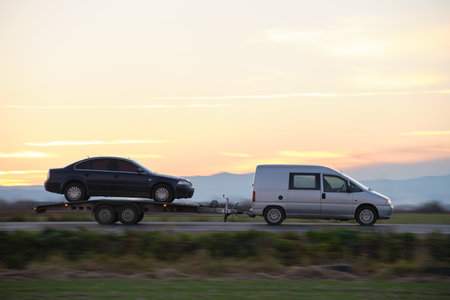 Tow truck vehicle with car transporting carrier trailer driving on highway in evening.の写真素材