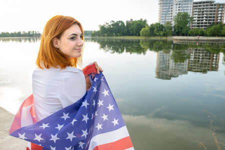 Young womanl holding USA national flag on her shoulders with high office buildings in a city celebrating United States independence dayの写真素材