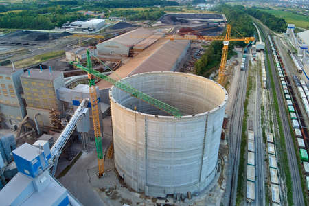 Aerial view of cement factory under construction with high concrete plant structure and tower cranes...