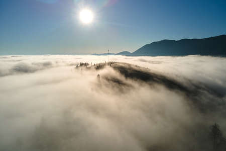 Aerial view of colorful sunrise over white dense fog with distant dark silhouettes of mountain hills on horizonの写真素材