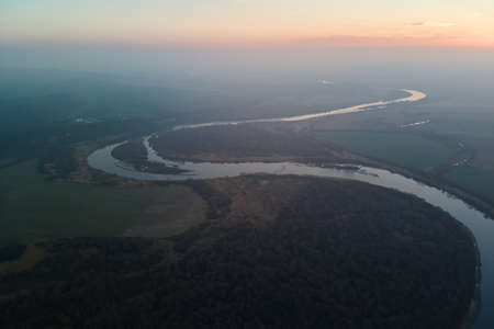 Aerial view of wide river flowing quietly in rural countryside in autumn evening
