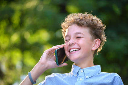 Happy young teenage boy talking on mobile phone outdoors in summer park. Online friendship conceptの写真素材