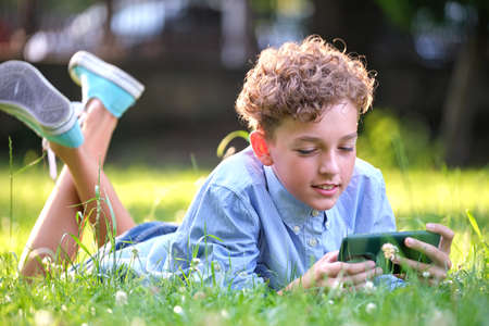 Young boy playing game on his smartphone outdoors in summer park. Addiction from electronic gadgets conceptの写真素材