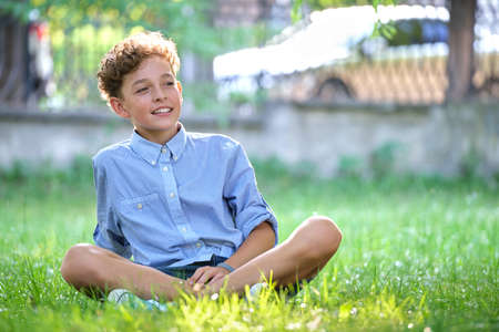 Young happy child boy relaxing on green grass in summer park. Positive kid enjoying summertime outdoors. Child wellbeing conceptの写真素材