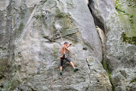 Young man climbing steep wall of rocky mountain. Male climber overcomes challenging route. Engaging...