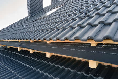 Closeup of house roof top covered with ceramic shingles. Tiled covering of building under...
