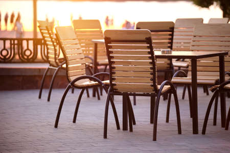 Closeup of outdoors cafe chairs and table at sunset on city streetの写真素材