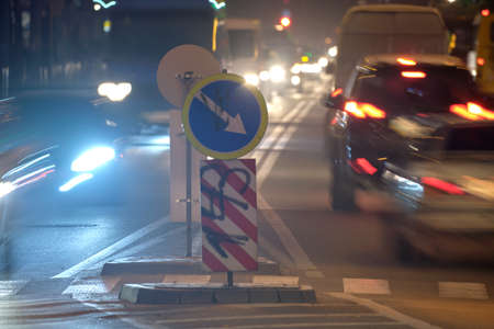 Direction road signs with blurred cars on city street traffic at night. Urban transportation concept