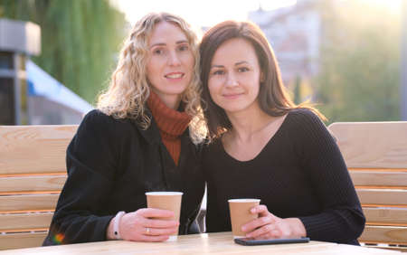 Happy businesswomen talking together during coffee break meeting at urban street cafe. Friendship...