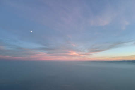 Aerial view of colorful sunset over white dense foggy clouds cover with distant dark silhouettes of...