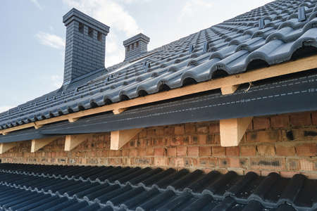 Closeup of house roof top covered with ceramic shingles. Tiled covering of building under...